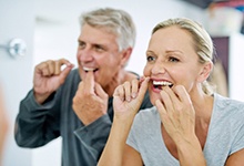 Man and woman flossing their teeth together