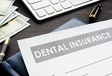 Dental insurance form resting on table next to keyboard and money